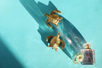 Photo of Decorative figures of turtles, perfume in bottles and beautiful shadow on light blue background, flat lay. Space for text