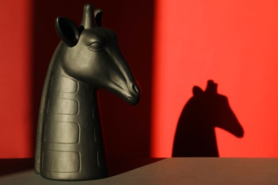 Photo of Decorative figure of giraffe on black table against red background with shadow