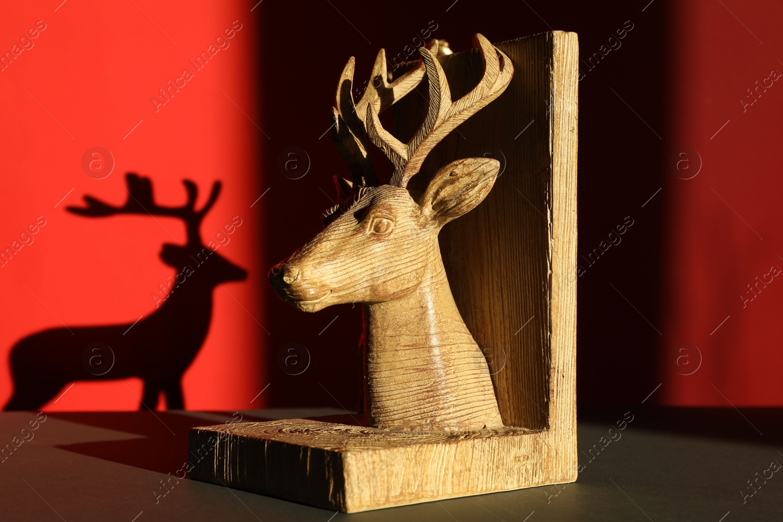 Photo of Decorative figure of deer on black table against red background with shadow