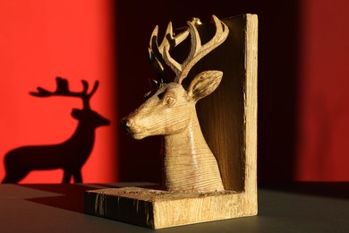 Photo of Decorative figure of deer on black table against red background with shadow