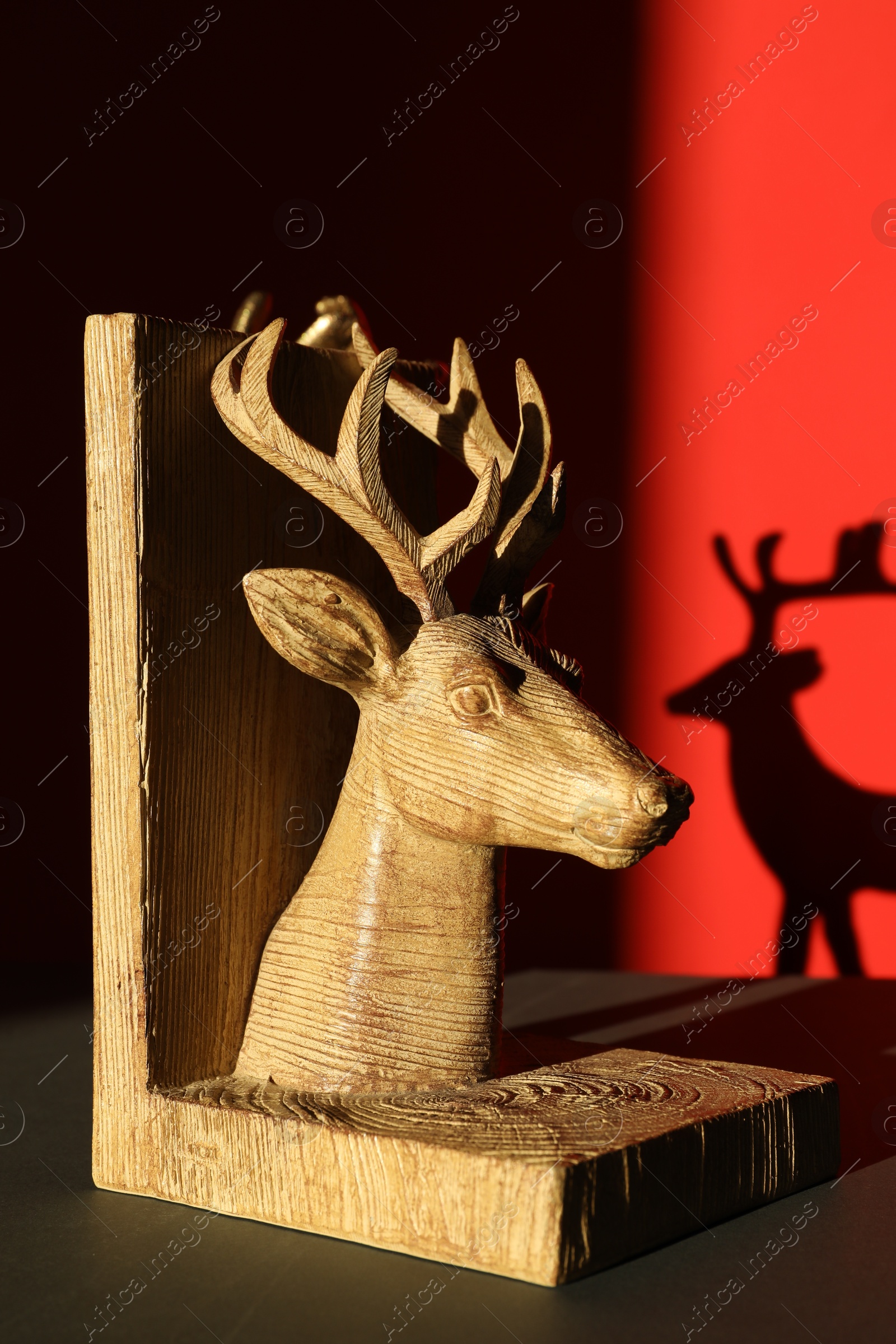 Photo of Decorative figure of deer on black table against red background with shadow