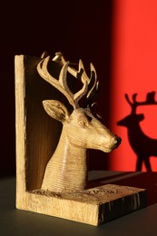 Photo of Decorative figure of deer on black table against red background with shadow