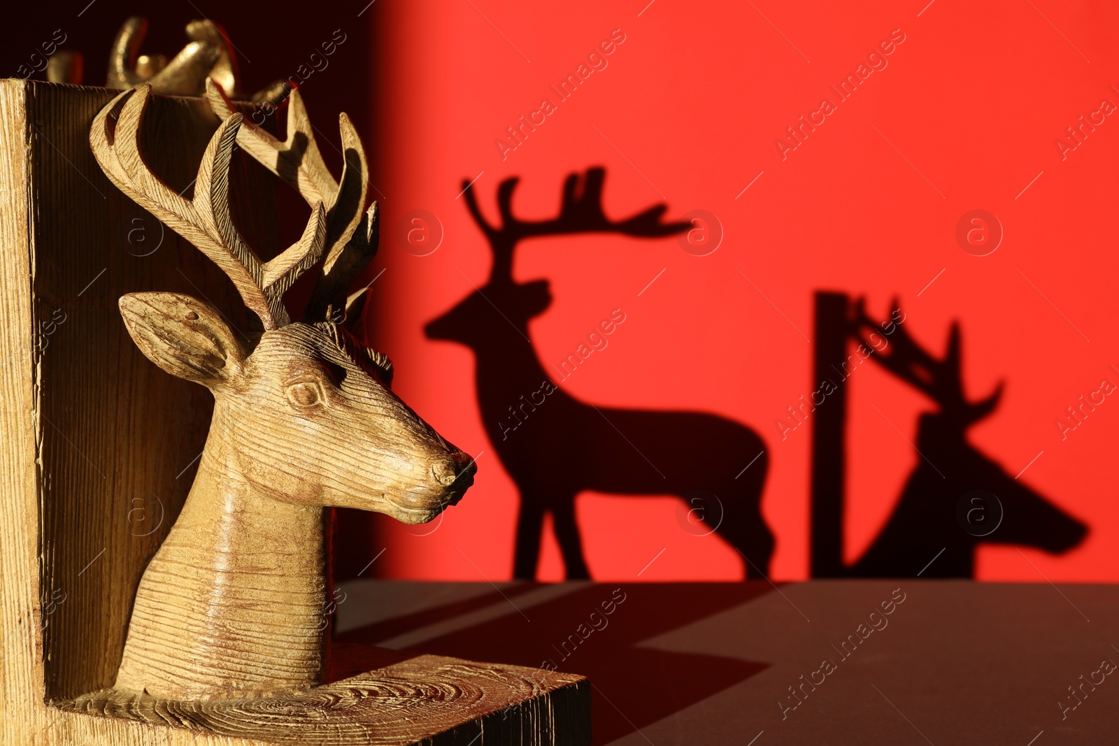 Photo of Decorative figure of deer on black table against red background with shadows