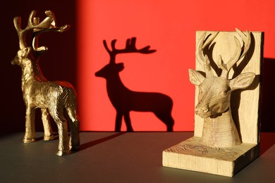 Photo of Decorative figures of deer on black table against red background with shadow