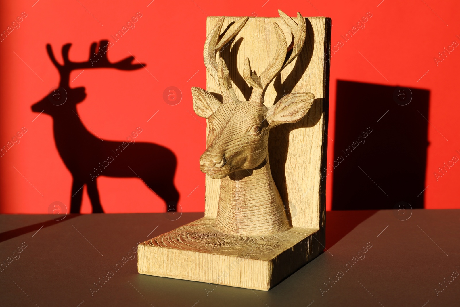 Photo of Decorative figure of deer on black table against red background with shadow