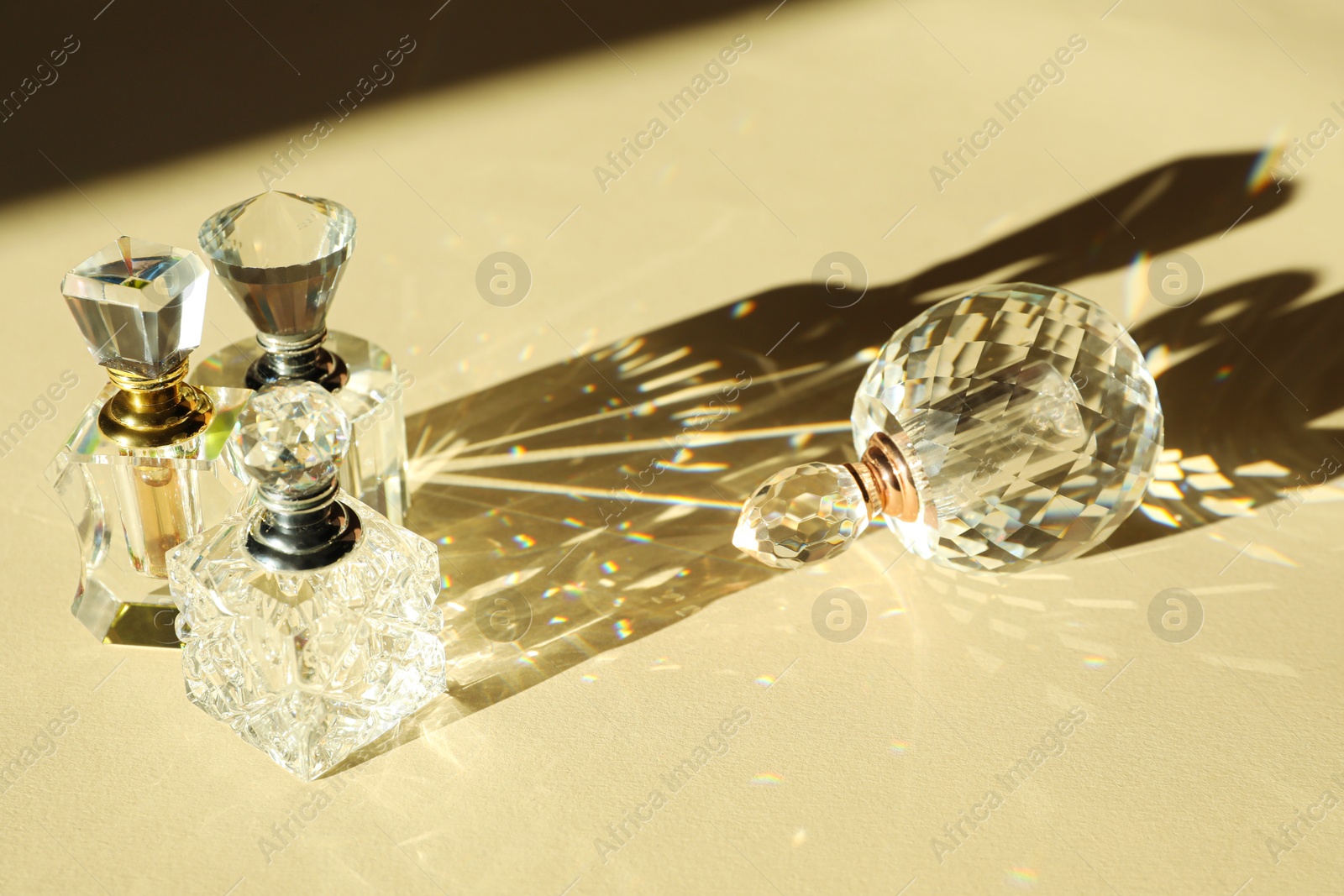 Photo of Many perfume bottles casting beautiful shadows on beige background, closeup