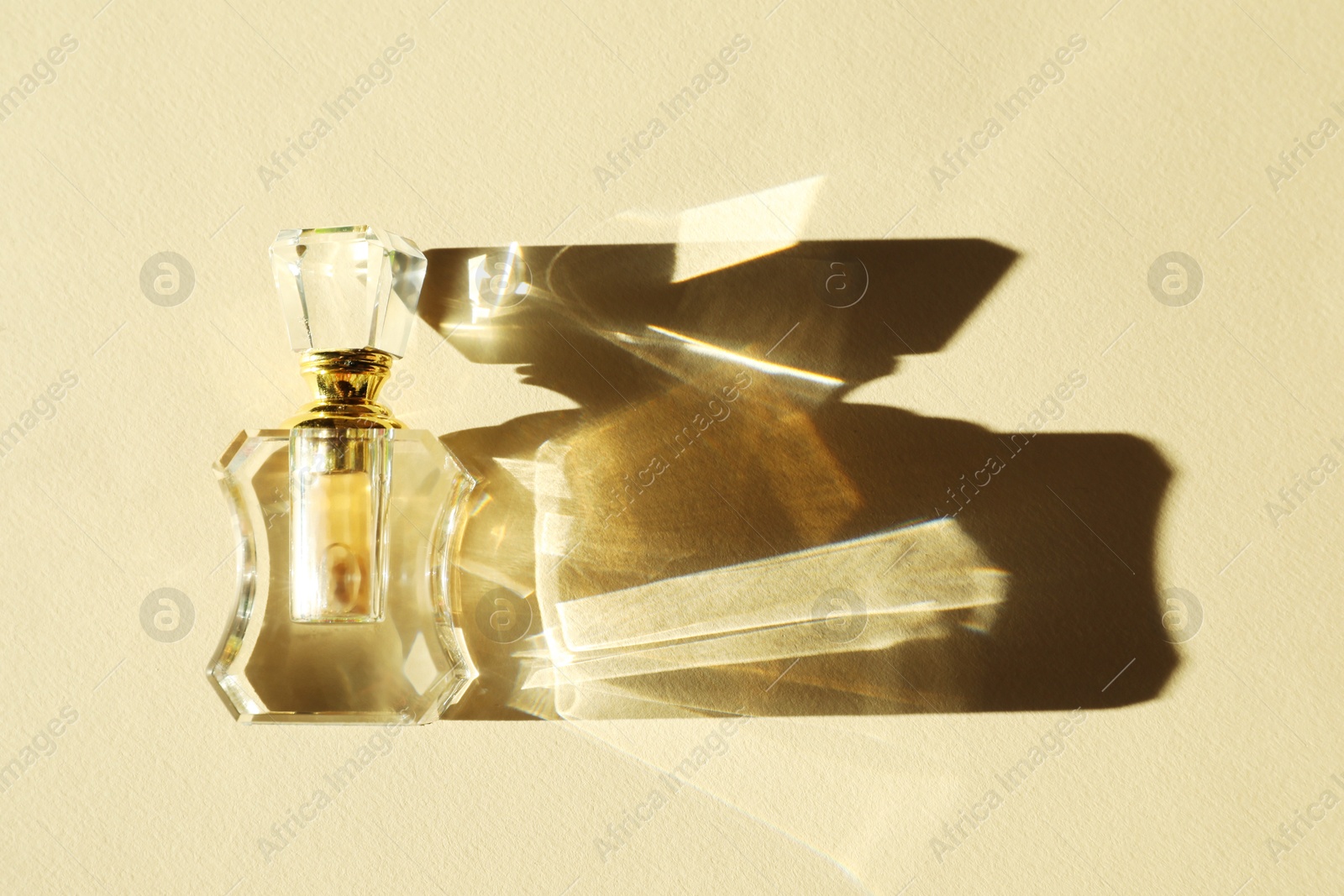 Photo of One perfume bottle casting beautiful shadow on beige background, top view