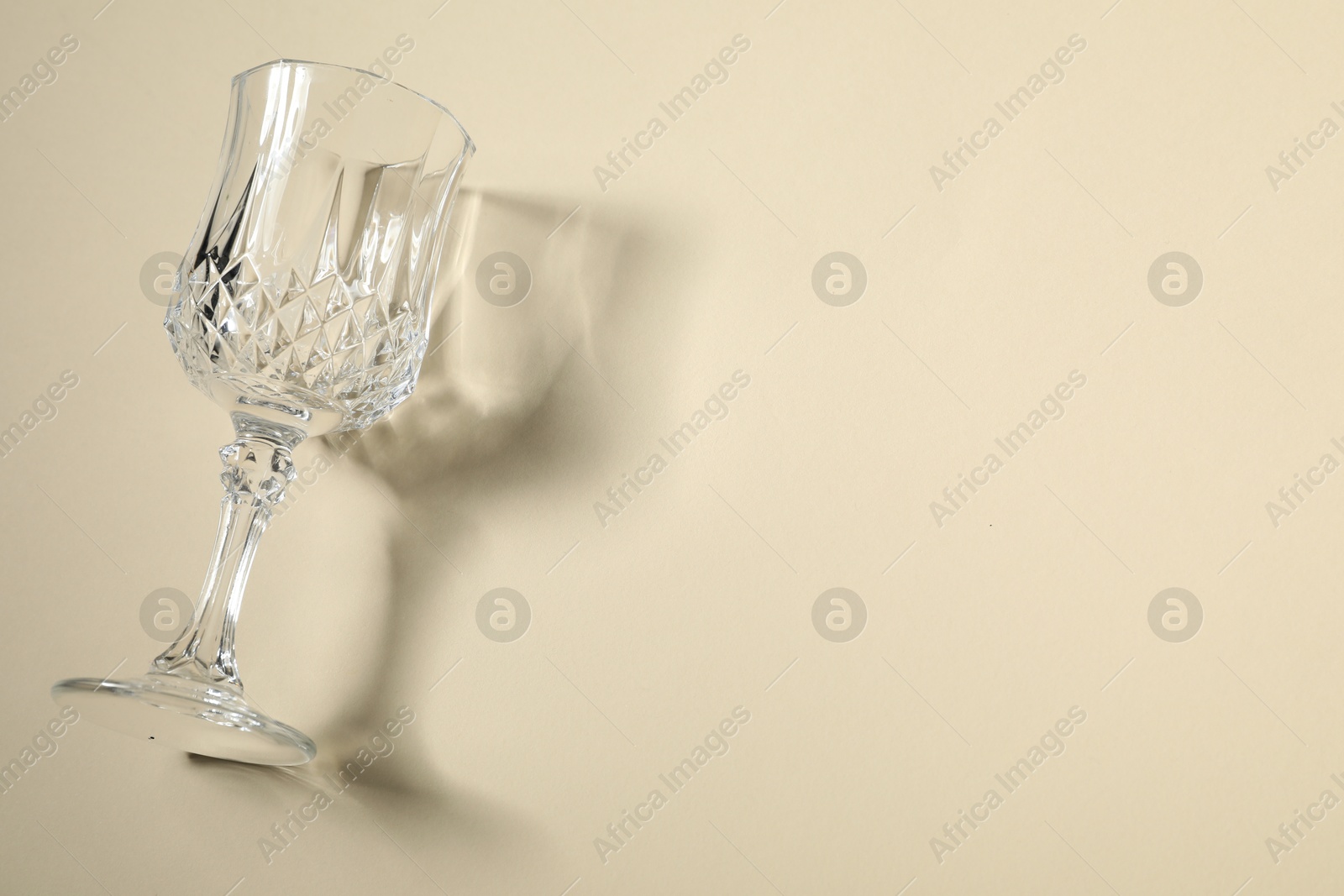 Photo of One empty wine glass casting beautiful shadow on beige background, top view. Space for text