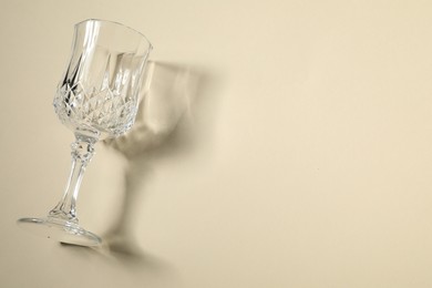 Photo of One empty wine glass casting beautiful shadow on beige background, top view. Space for text