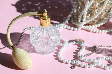 Photo of Bottle of perfume and stylish jewelry on pink background with shadows