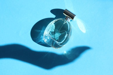 Photo of Perfume bottle and shadow of woman's hand on light blue background, top view