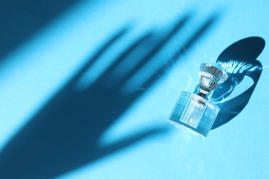 Photo of Perfume bottle and shadow of woman's hand on light blue background, top view