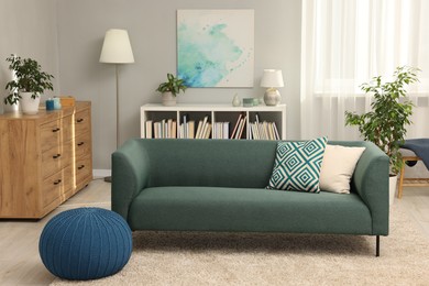 Photo of Stylish living room interior with soft sofa, pouf, houseplants and chest of drawers near grey wall