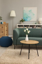 Photo of Soft sofa, coffee table, pouf, houseplants and chest of drawers near grey wall in living room. Interior design