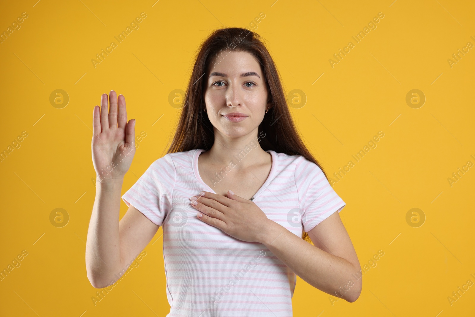 Photo of Woman making promise with raised hand on orange background. Oath gesture