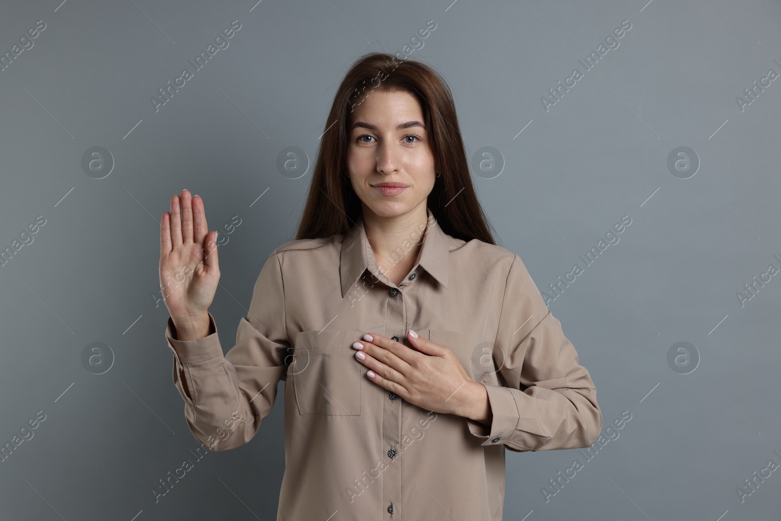 Photo of Woman making promise with raised hand on grey background. Oath gesture