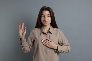 Photo of Woman making promise with raised hand on grey background. Oath gesture