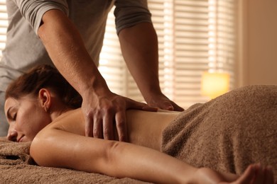 Photo of Osteopath massaging woman's back on couch indoors, closeup. Manual therapy