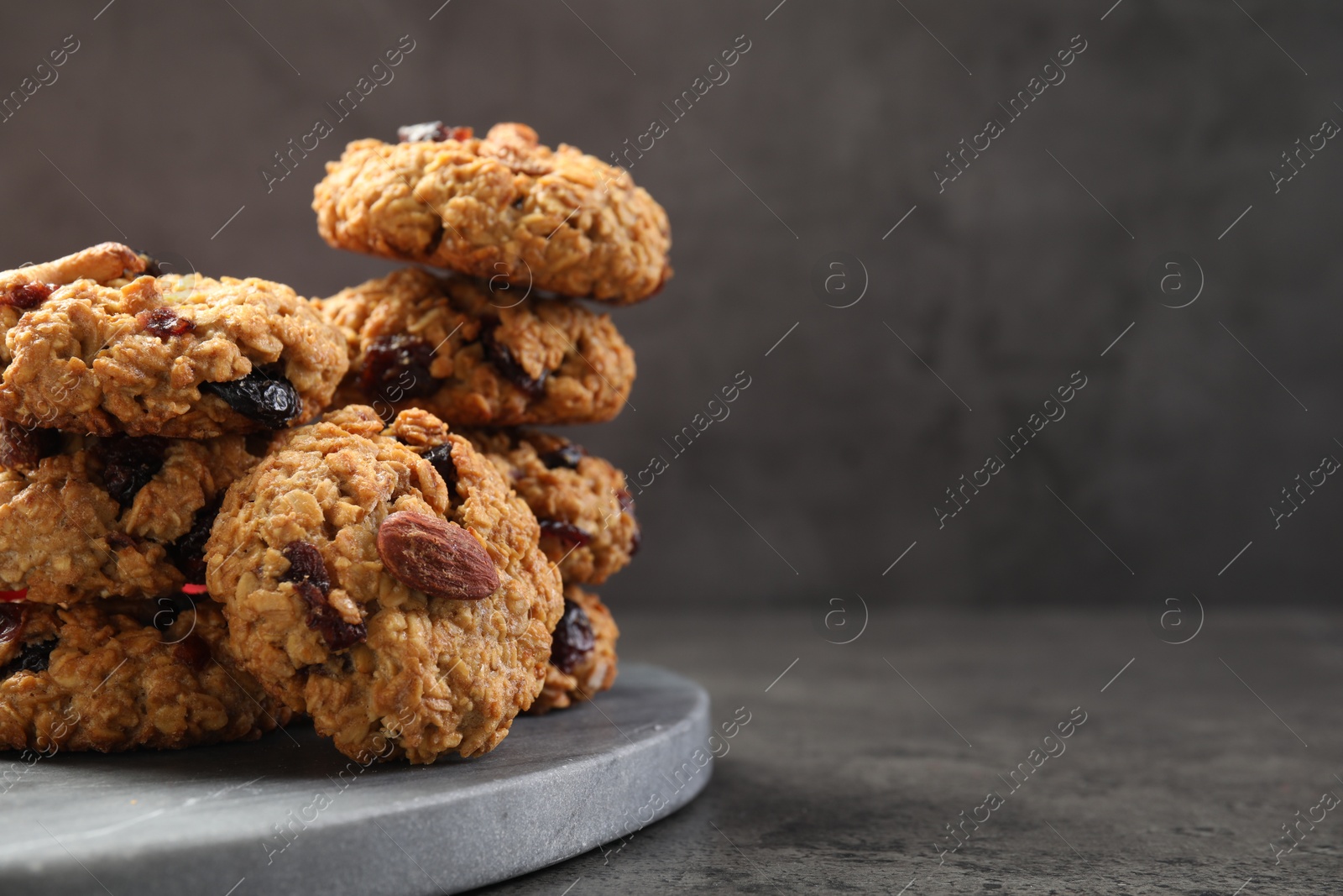 Photo of Delicious oatmeal cookies with raisins and nuts on grey table, closeup. Space for text