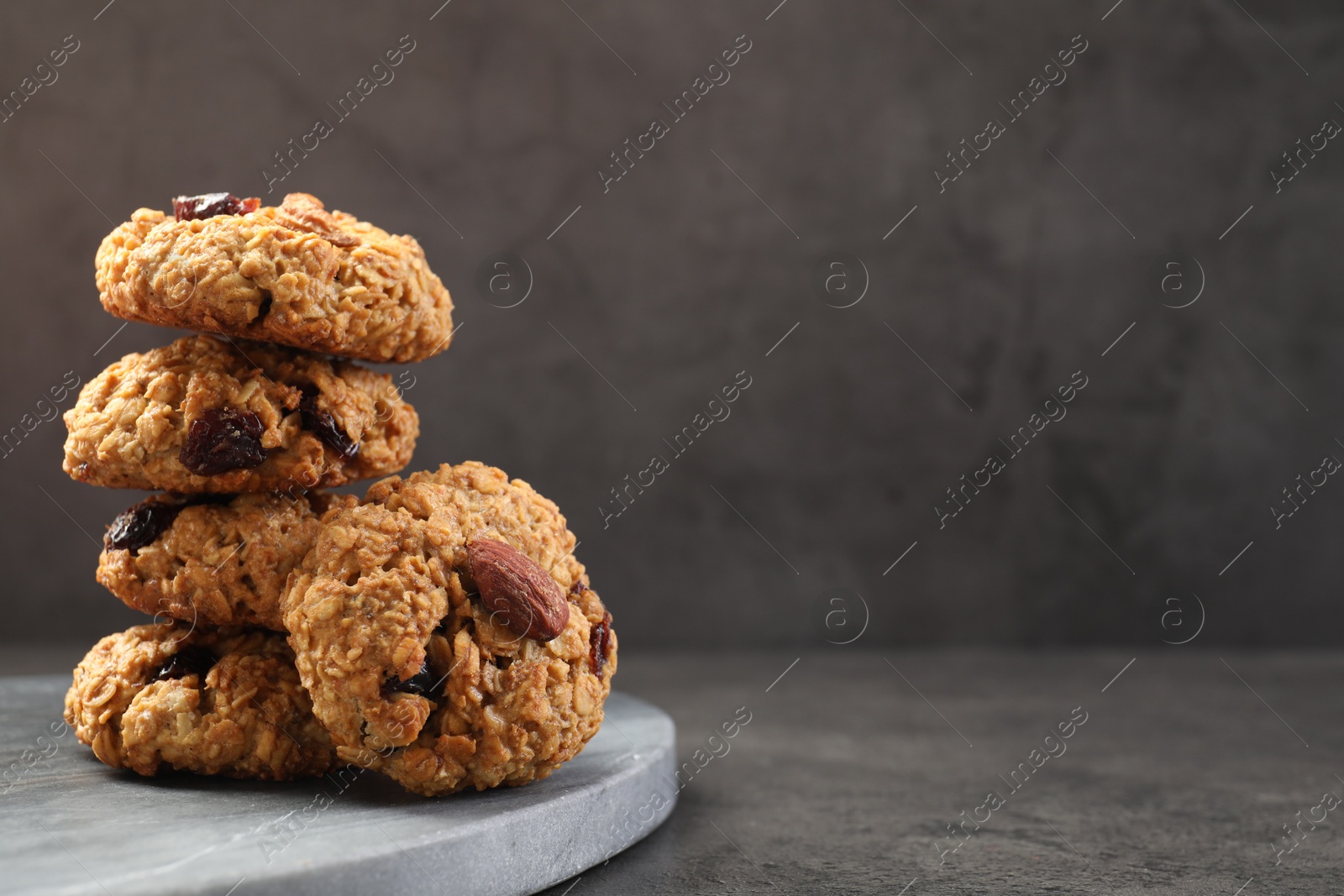 Photo of Delicious oatmeal cookies with raisins and nuts on grey table, closeup. Space for text