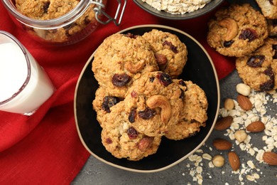 Delicious oatmeal cookies with raisins, nuts and ingredients on grey table, flat lay