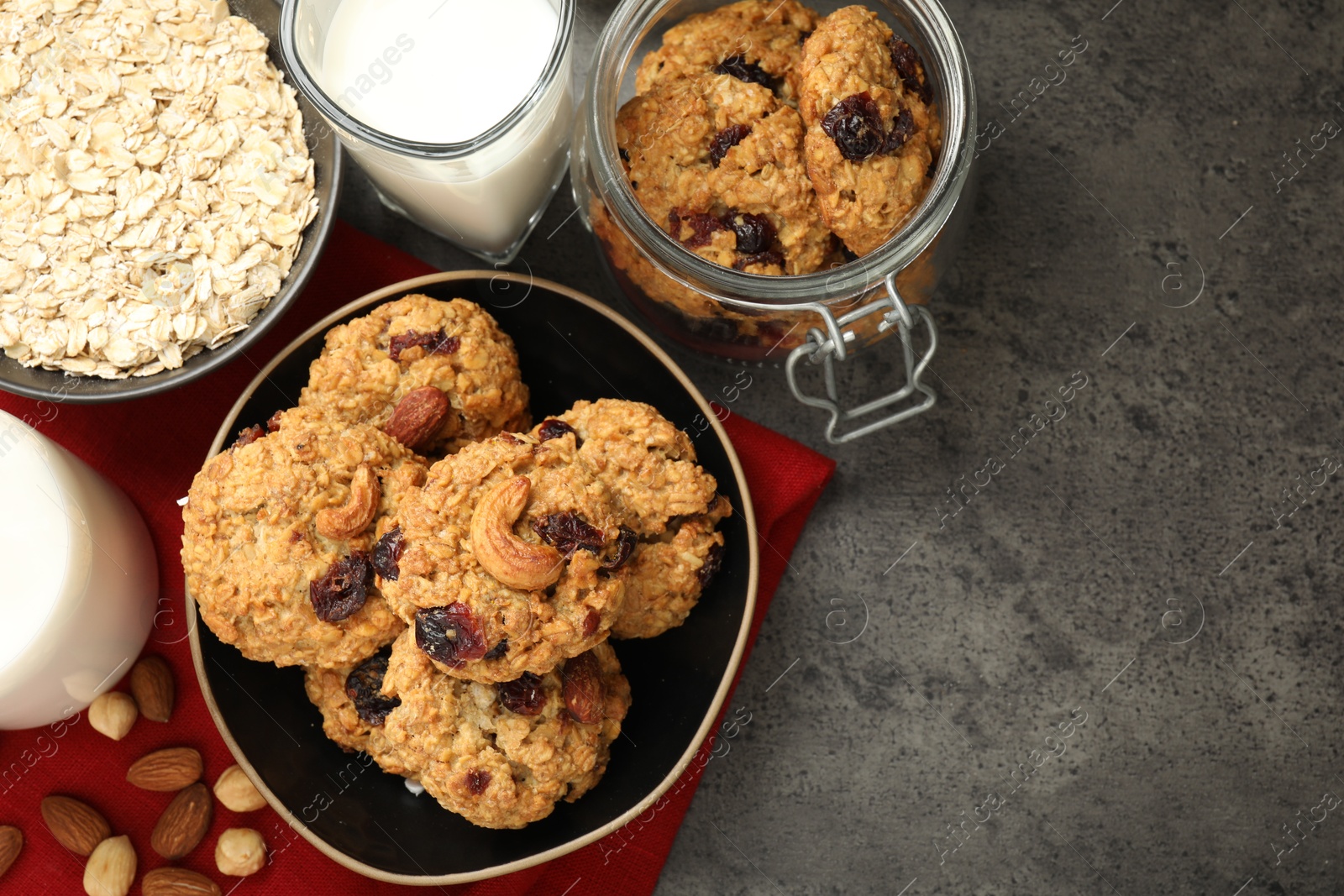 Photo of Delicious oatmeal cookies with raisins, nuts and ingredients on grey table, flat lay. Space for text