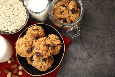 Photo of Delicious oatmeal cookies with raisins, nuts and ingredients on grey table, flat lay. Space for text