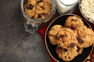 Photo of Delicious oatmeal cookies with raisins, nuts and ingredients on grey table, flat lay. Space for text