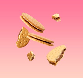 Image of Tasty broken sandwich cookies in air on pink gradient background