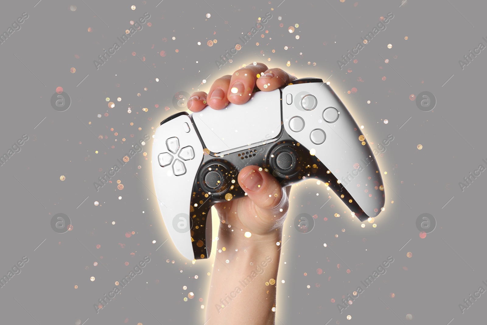 Image of Woman holding game controller on grey background, closeup. Glow around hand and shiny sparkles