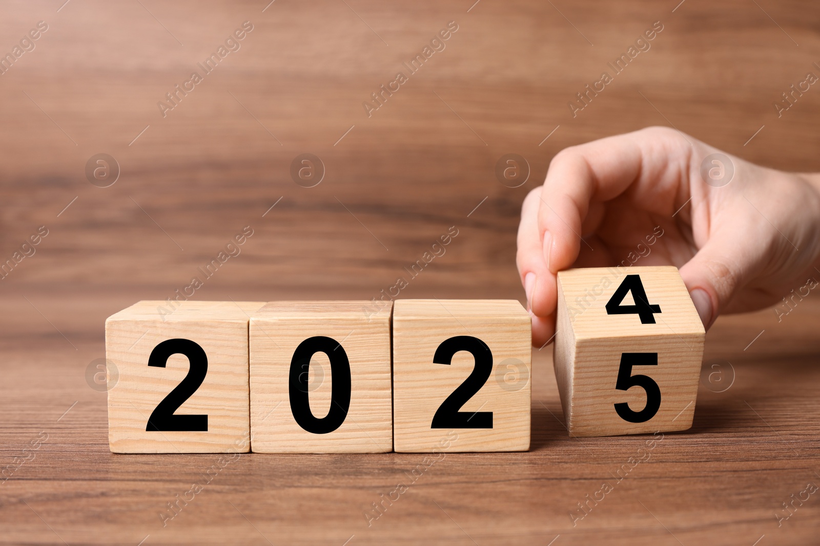 Image of 2025 New Year. Woman turning wooden cube on table, closeup