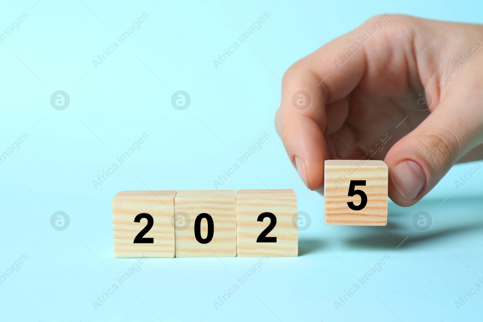 Image of 2025 New Year. Woman putting wooden cube with number 5 on light blue background, closeup