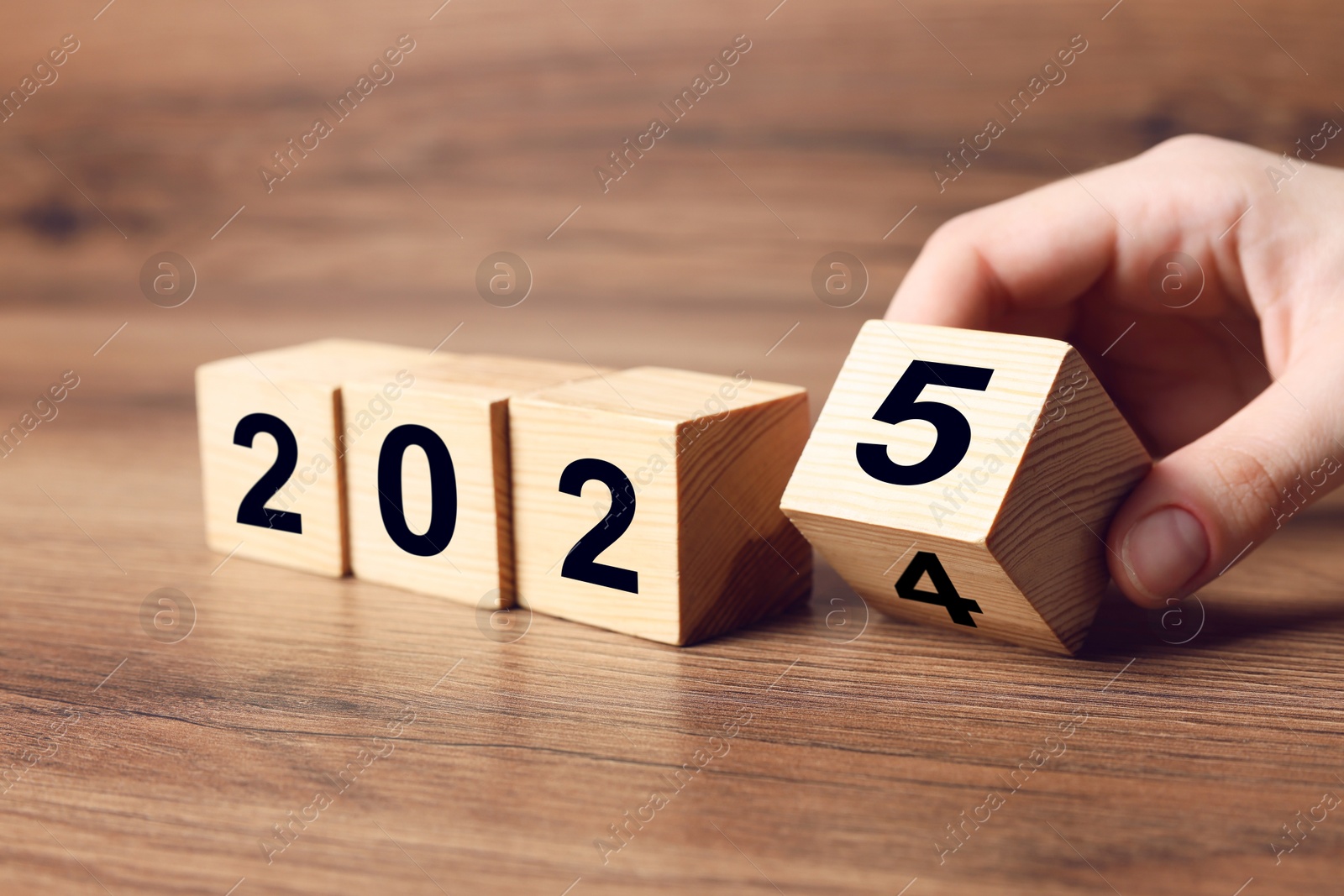 Image of 2025 New Year. Woman turning wooden cube on table, closeup