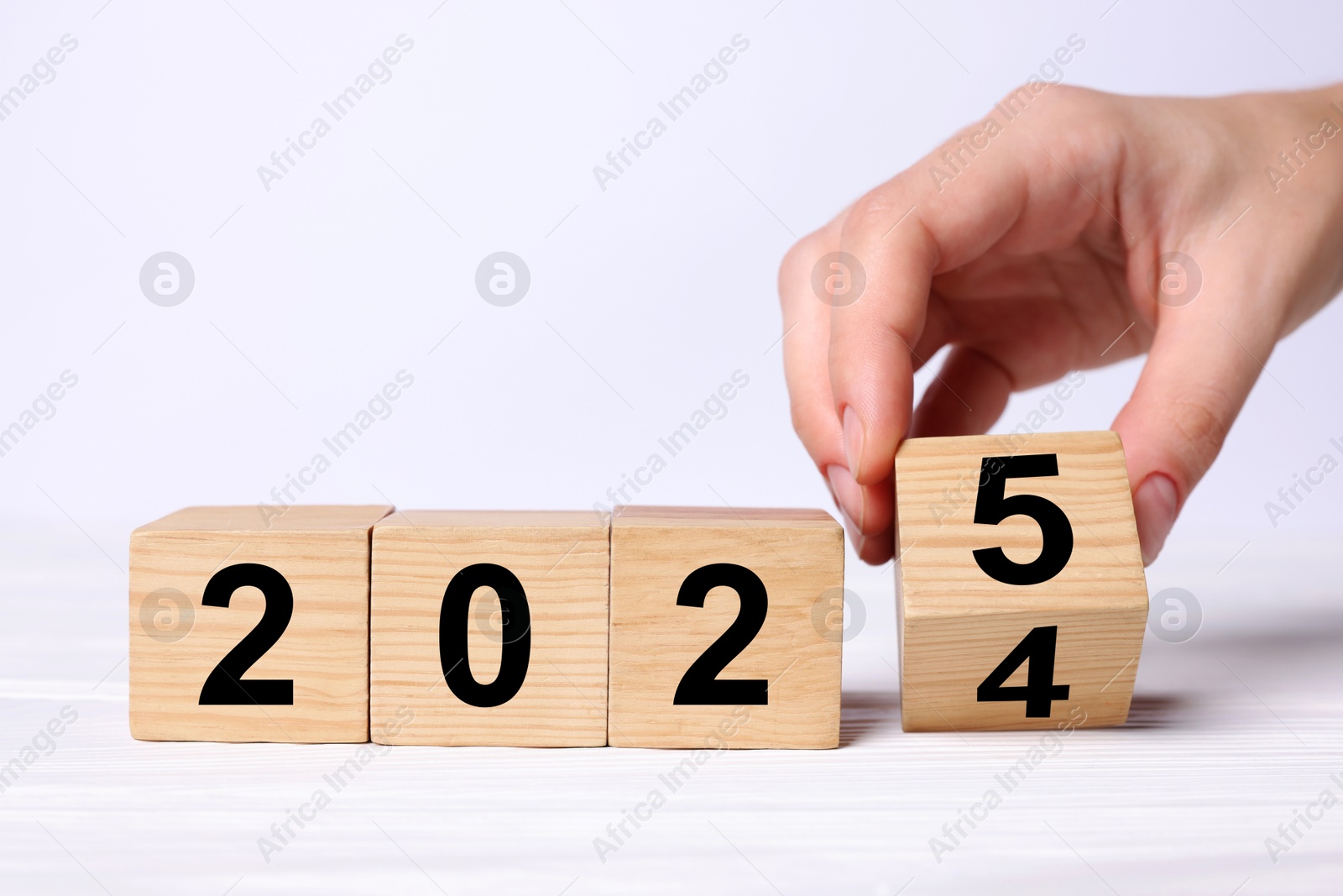 Image of 2025 New Year. Woman turning wooden cube on white table, closeup