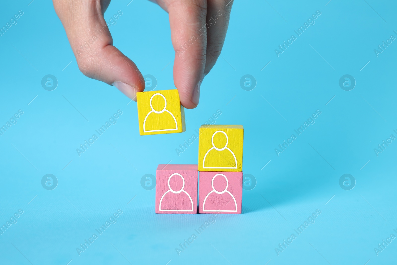 Image of Human resource. Woman stacking wooden cubes with human icons on light blue background, closeup