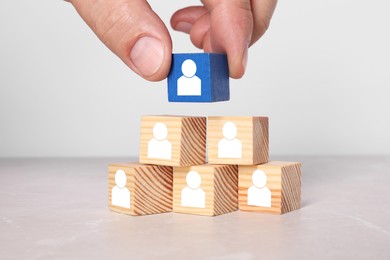 Human resource. Woman stacking pyramid of wooden cubes with human icons on white table, closeup