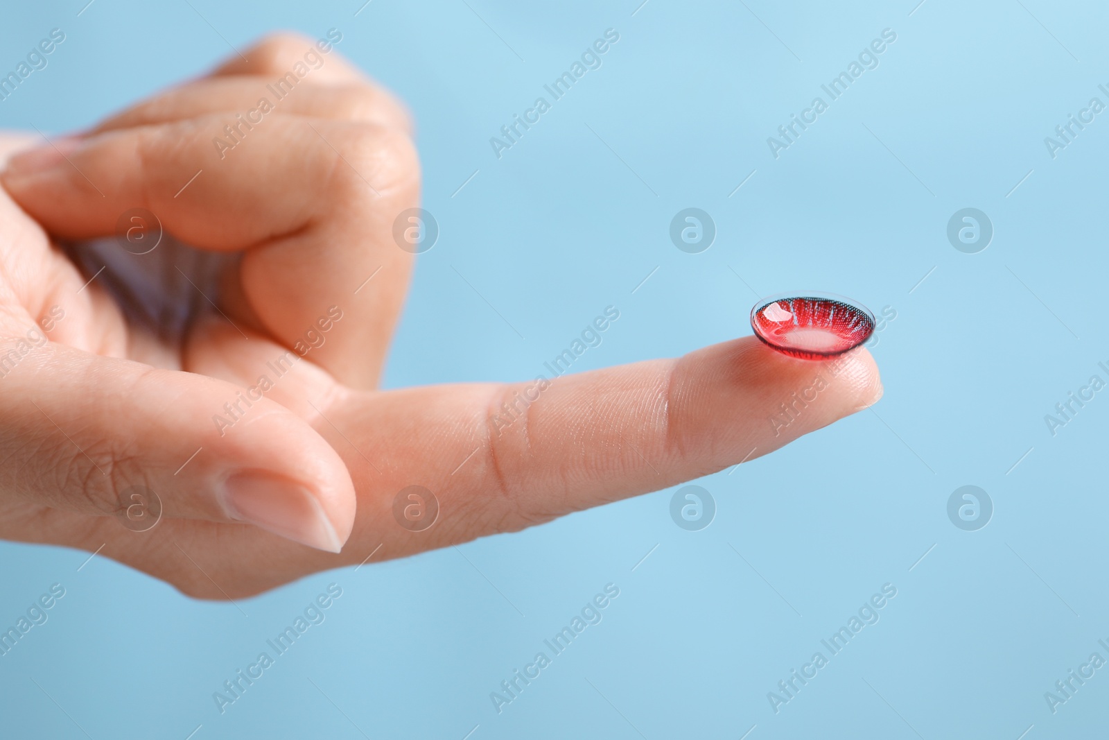 Photo of Woman holding color contact lens on light blue background, closeup