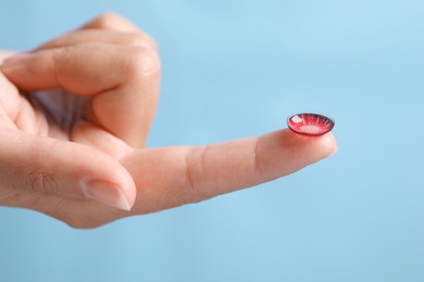 Photo of Woman holding color contact lens on light blue background, closeup