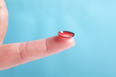 Woman holding color contact lens on light blue background, closeup