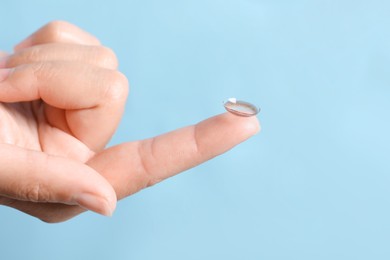 Photo of Woman holding color contact lens on light blue background, closeup