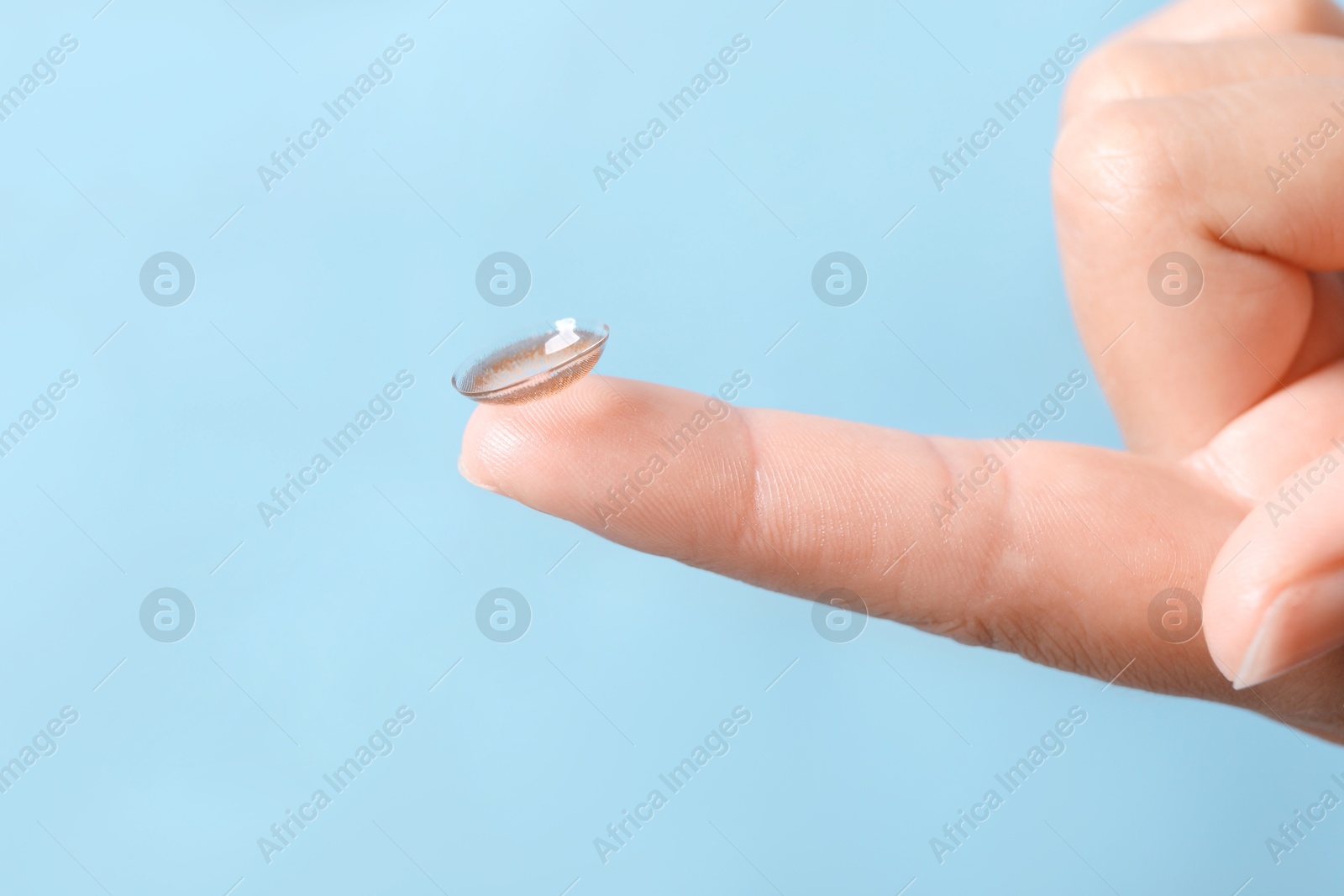 Photo of Woman holding color contact lens on light blue background, closeup