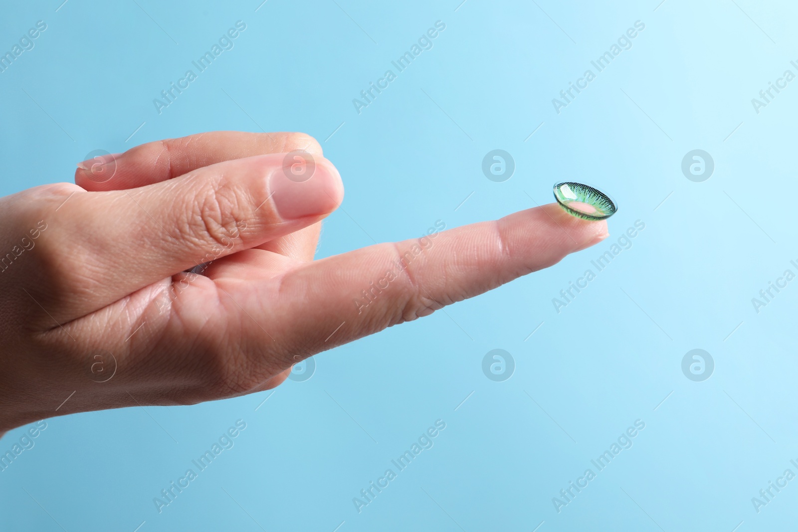 Woman holding color contact lens on light blue background, closeup Photo of Woman holding color contact lens on light blue background, closeup