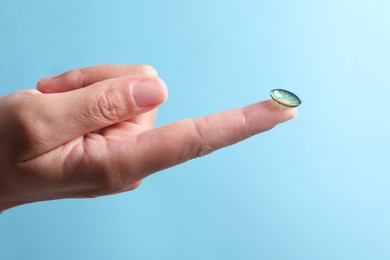 Photo of Woman holding color contact lens on light blue background, closeup