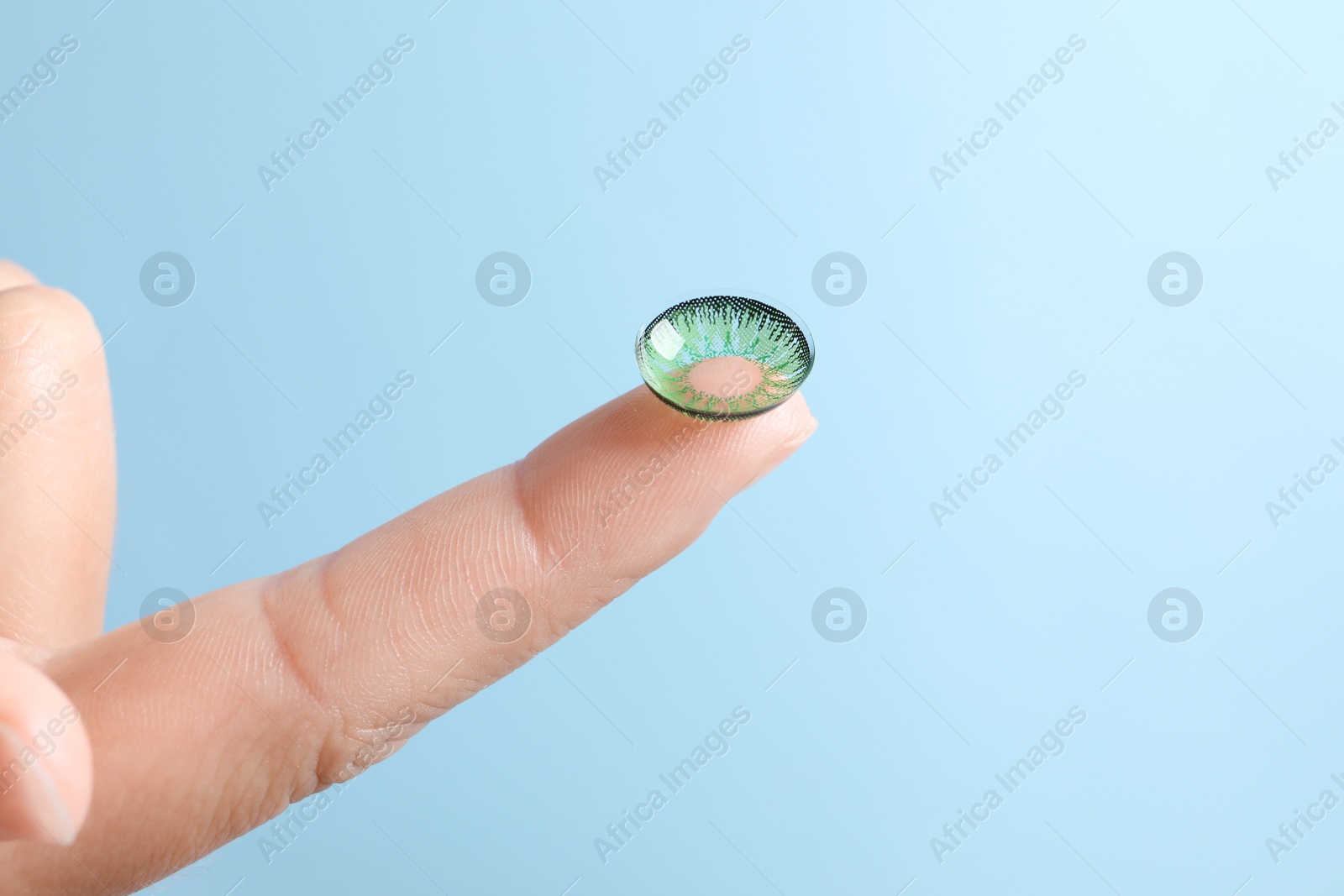 Photo of Woman holding color contact lens on light blue background, closeup