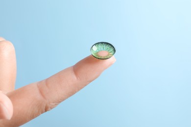 Photo of Woman holding color contact lens on light blue background, closeup