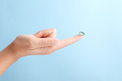 Photo of Woman holding color contact lens on light blue background, closeup