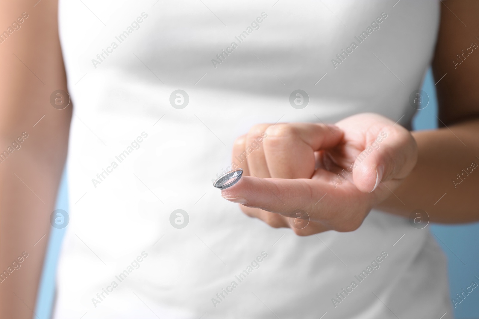 Woman holding color contact lens on light blue background, closeup Photo of Woman holding color contact lens on light blue background, closeup
