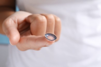 Photo of Woman holding color contact lens on light blue background, closeup