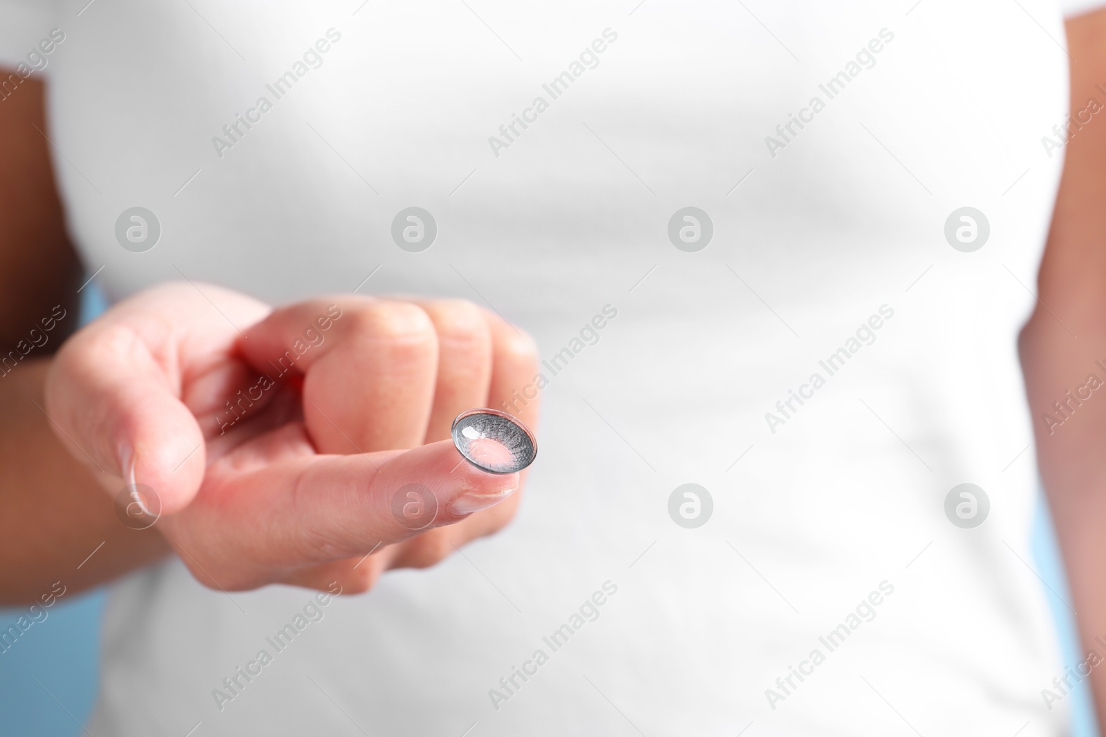 Woman holding color contact lens on light blue background, closeup Photo of Woman holding color contact lens on light blue background, closeup
