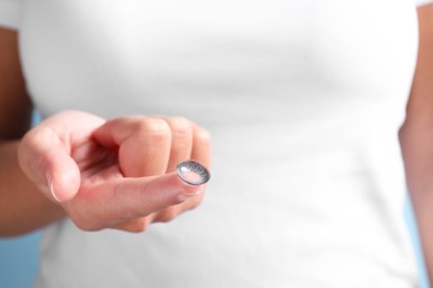 Photo of Woman holding color contact lens on light blue background, closeup